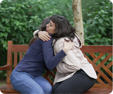 two persons who are hugging each other while sitting on a bench